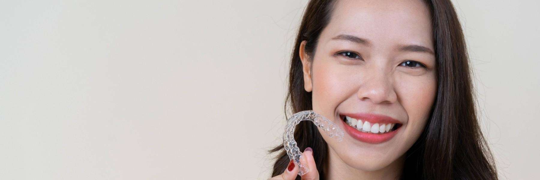 A smiling woman holding her clear aligners in Armidale NSW