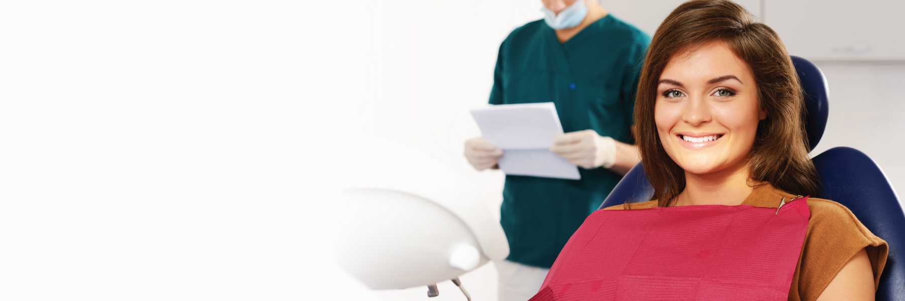 Smiling woman in dental chair with dentist reviewing treatment notes behind her